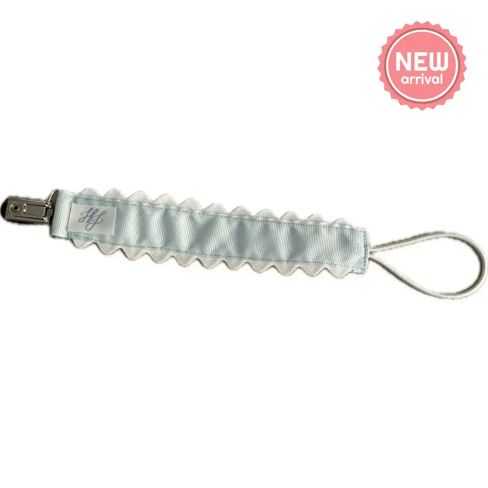 Hampton James Blue Paci Clip attached to a baby pacifier, featuring a durable clip and soft blue fabric for gentle baby use.