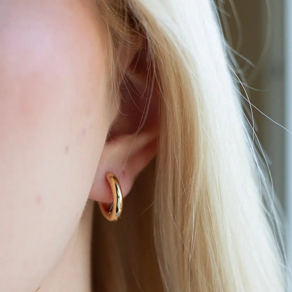 Lenny & Eva tarnish resistant gold hoop huggie earrings, close-up of round, shiny gold earrings with a secure clasp.