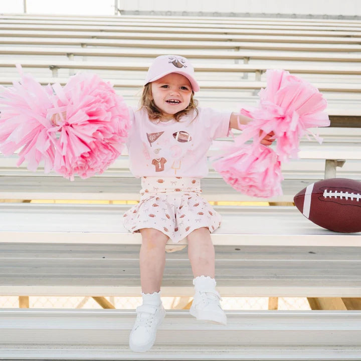 Model wearing Sweet Wink Game Day Athletic Skort paired with a football-themed short sleeve t-shirt and baseball hat.
