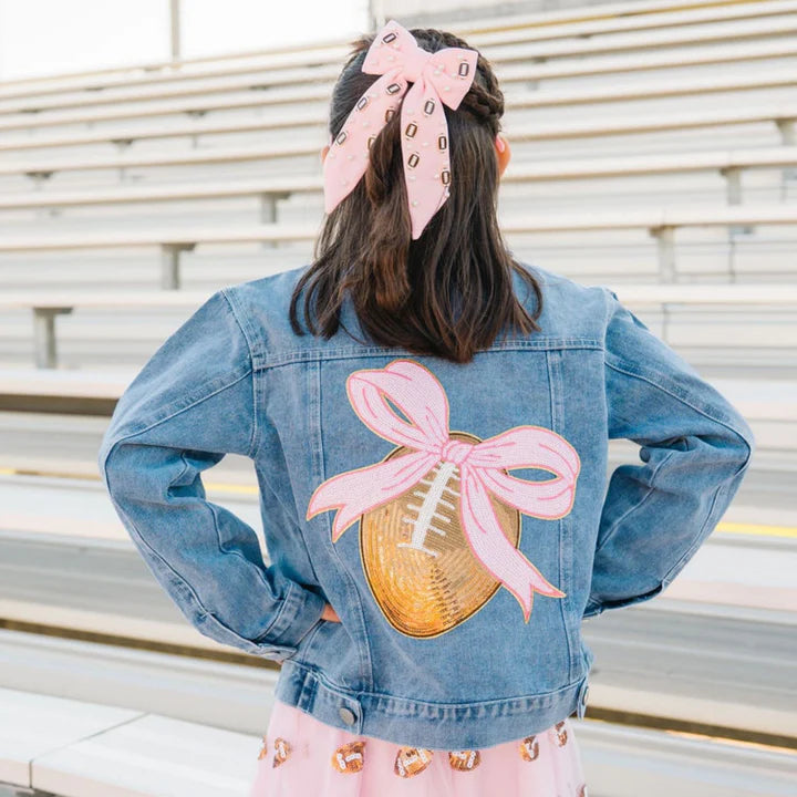 Model wearing a denim jacket with a football pearl bow clip featuring football sequin patch by Sweet Wink.