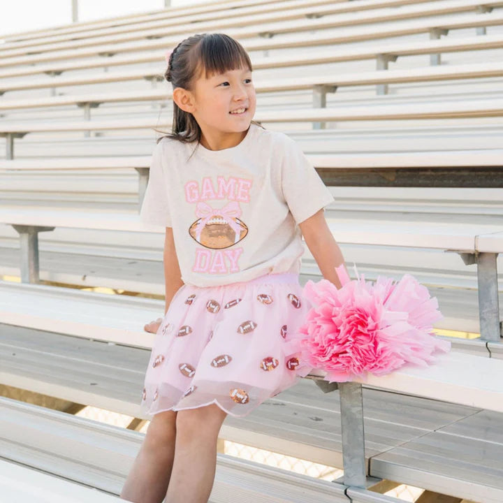 Model wearing Sweet Wink mini sequin footballs tutu skirt with pearl bow clip, paired with a short sleeve game day sequin patch t-shirt.