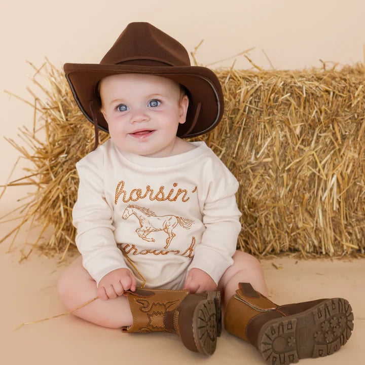 Girl wearing the Horsin' Around Western Long Sleeve Romper by Sweet Wink, featuring a western-inspired design and long sleeves.