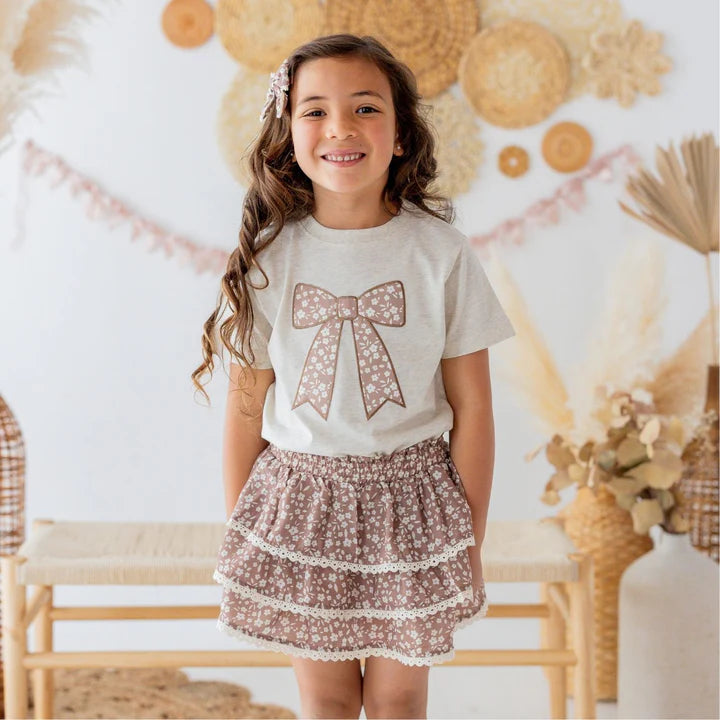 Model wearing a mocha floral skort by Sweet Wink paired with a short sleeve t-shirt and lace bow clip.