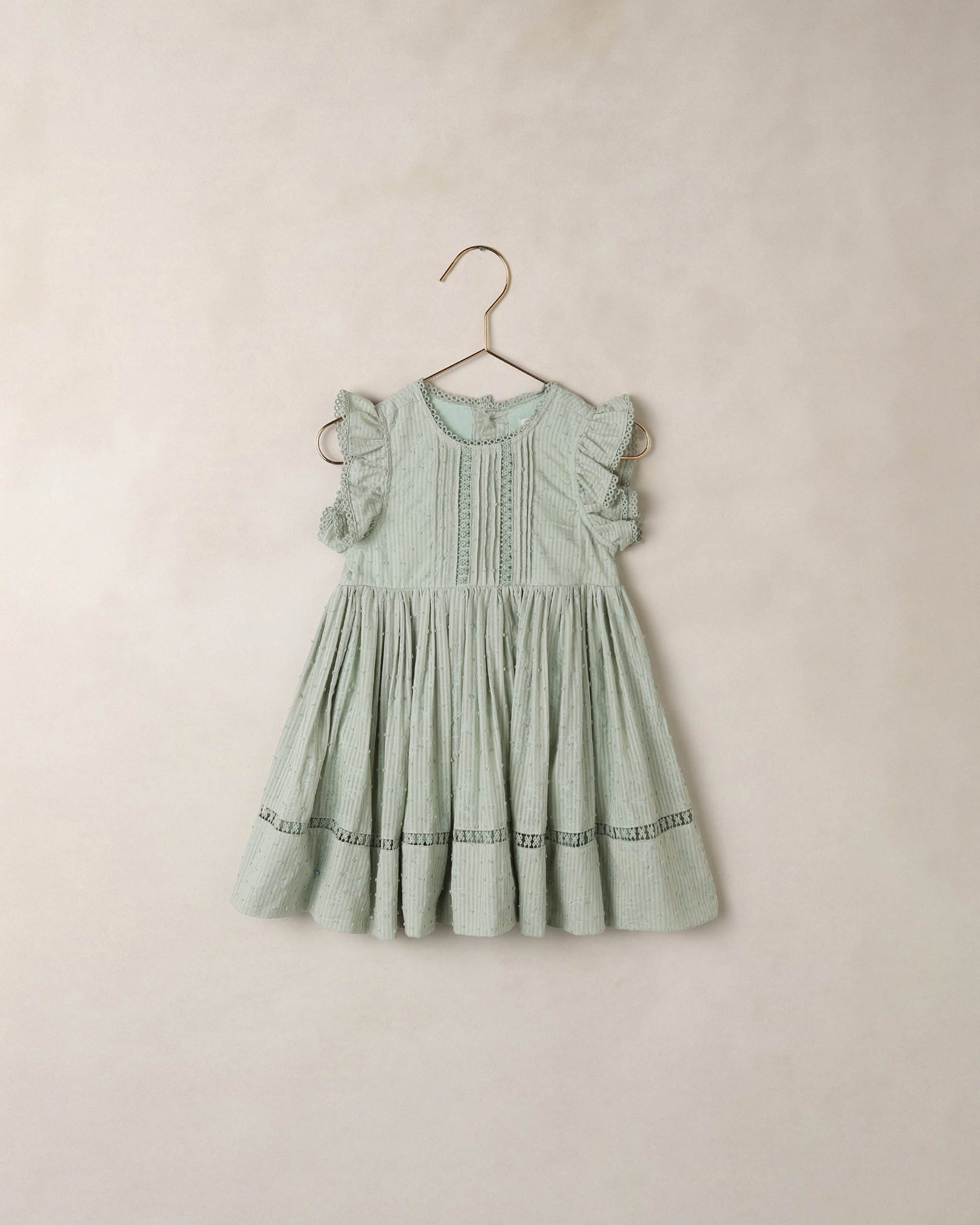 Noralee Eucalyptus Isla Dress shown hanging on a wooden hanger with a flowy, lightweight fabric and botanical print.