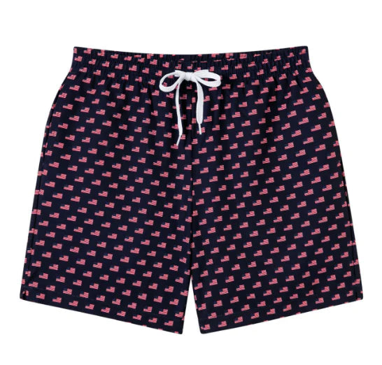 Meripex Old Glory swim trunks featuring a patriotic flag design, displayed on a hanger with a colorful beach background.