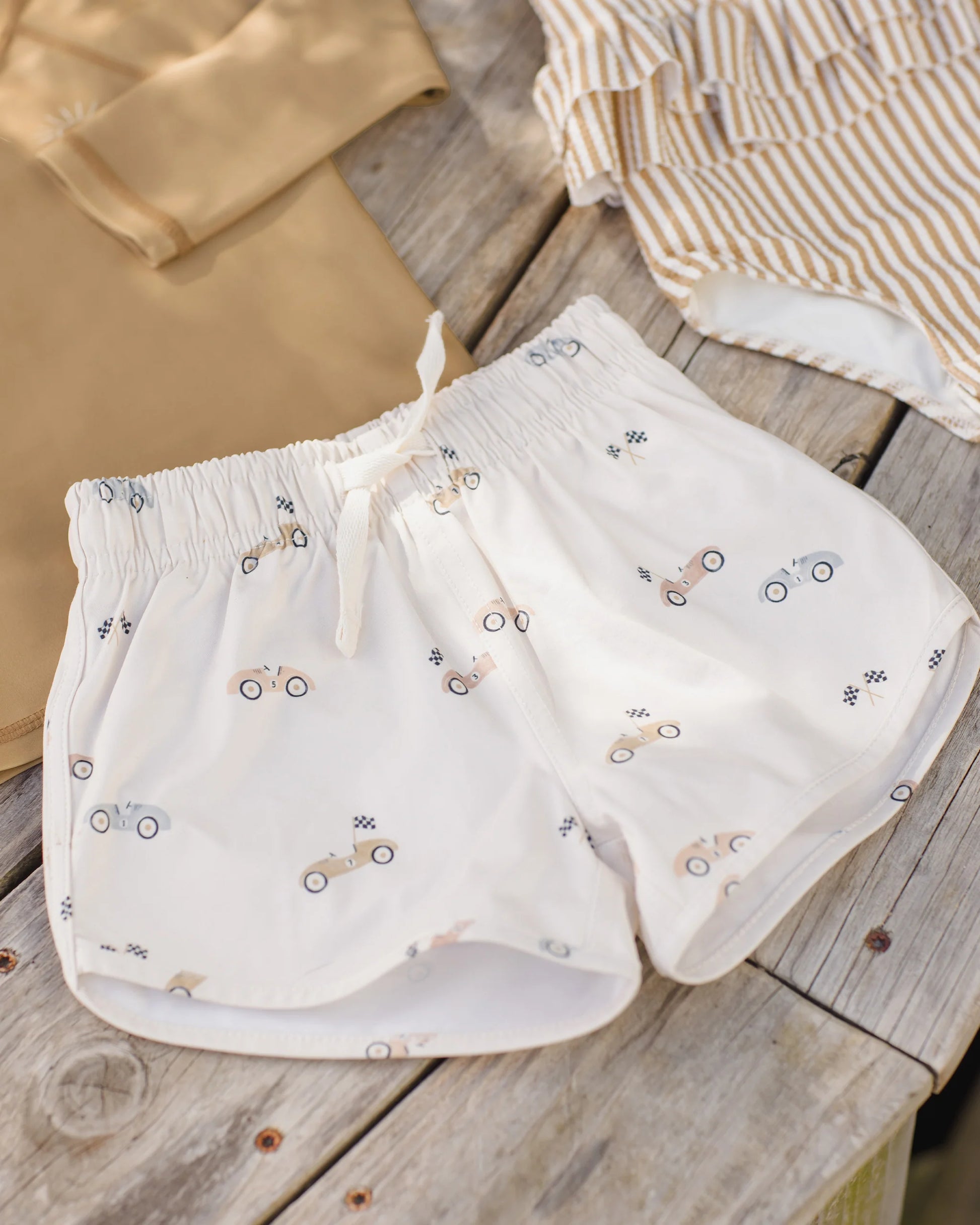 Boy wearing Quincy Mae race car boys swim shorts, featuring colorful race car print, casual summer swimwear for kids.
