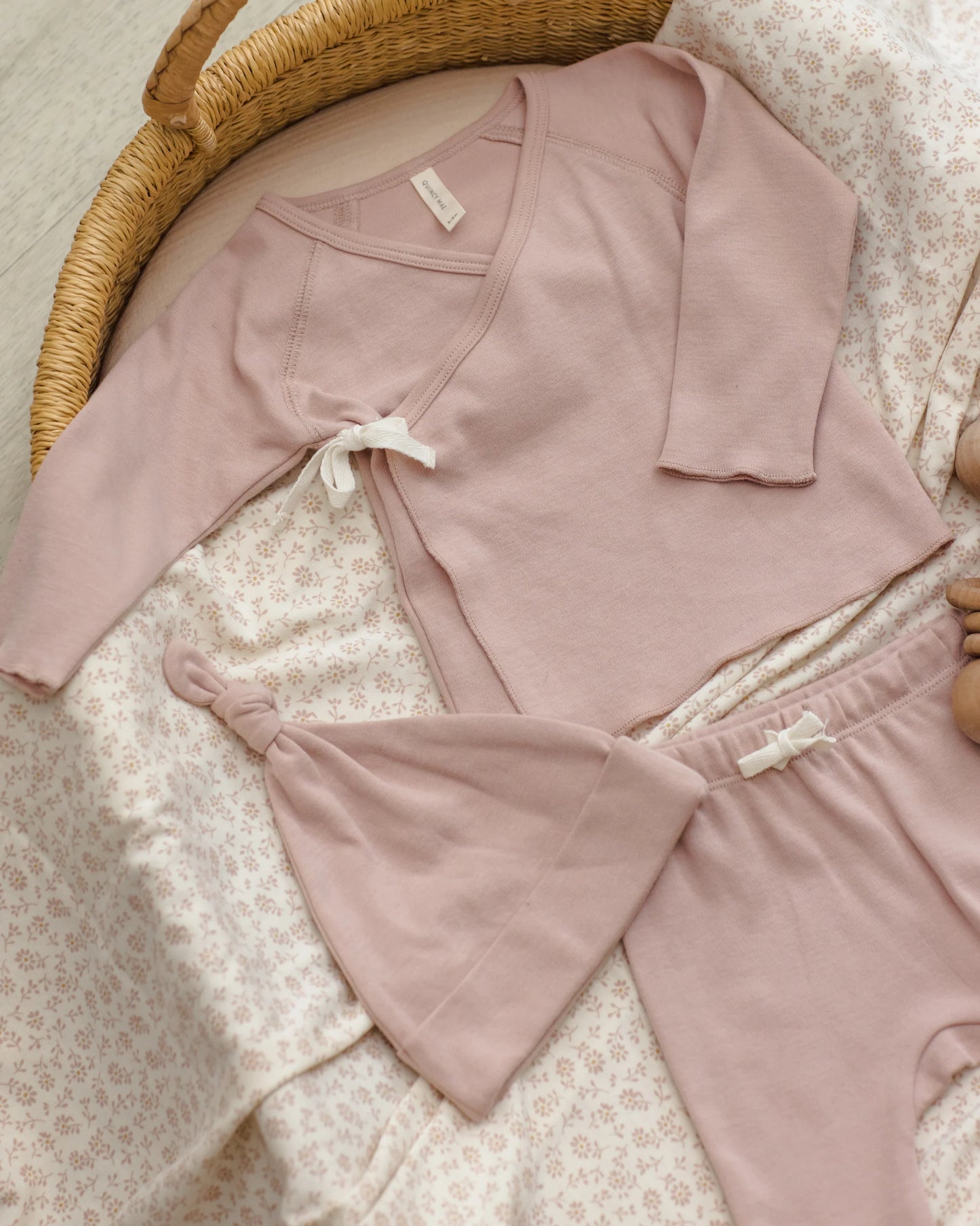 Baby wearing a blush pink knotted baby hat by Quincy Mae, styled in a cozy lifestyle setting.