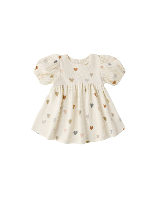 Confetti Hearts Darla Dress by Quincy Mae, natural-colored dress with colorful heart patterns, displayed hanging on a white background.