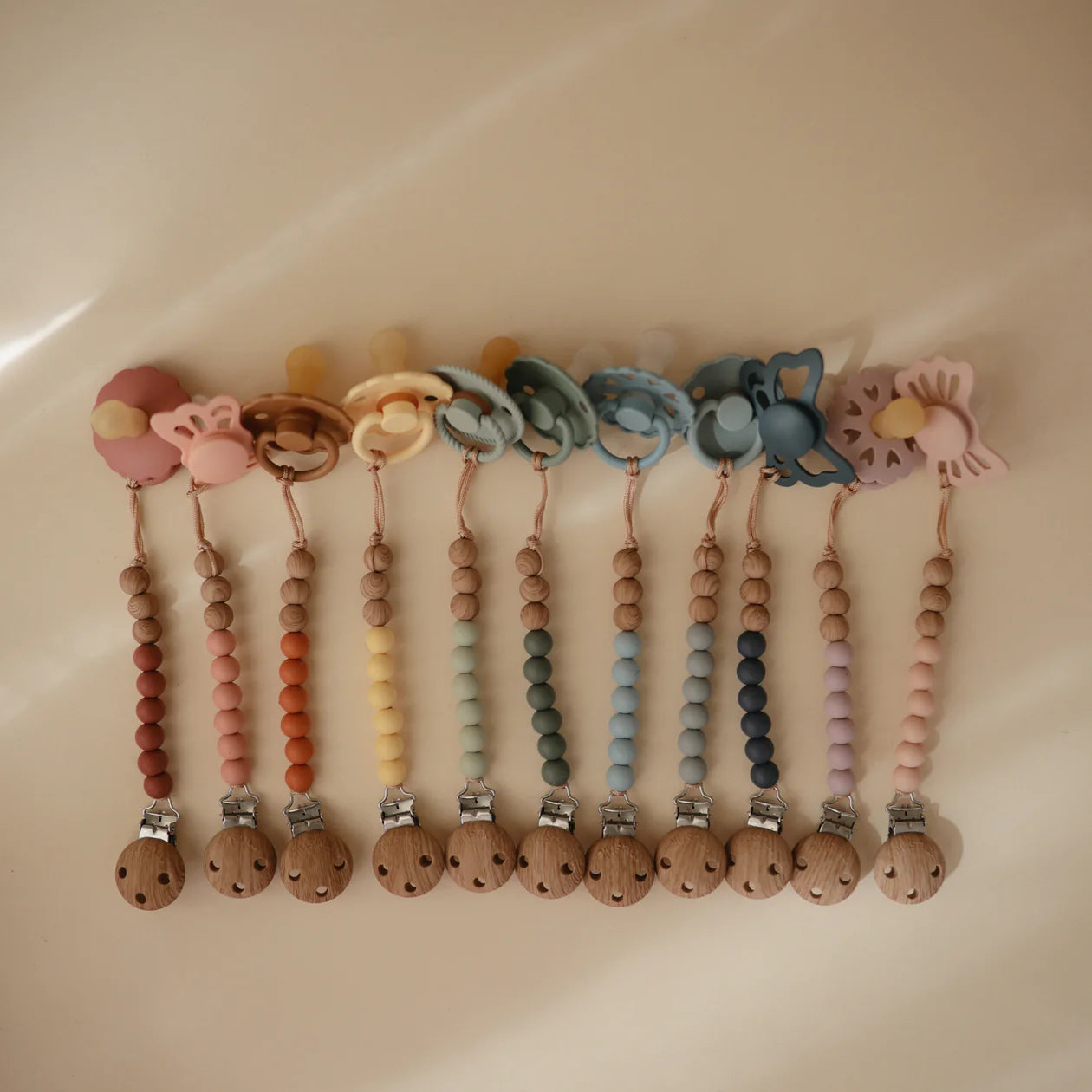 Mushie silicone pacifier clip with pastel-colored beads and clip attachment, designed to keep pacifiers secure and stylish.